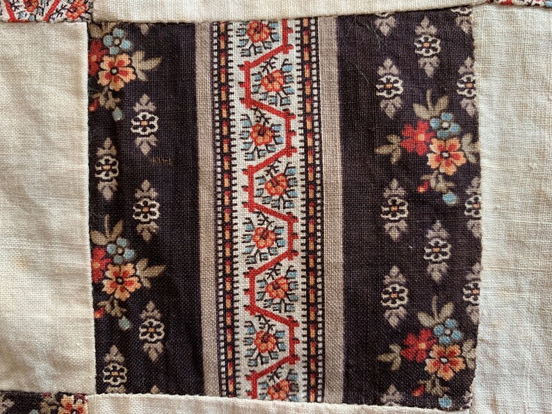 May include: A close-up of a fabric patchwork with a brown and white floral pattern, a red and white geometric pattern, and a beige background.