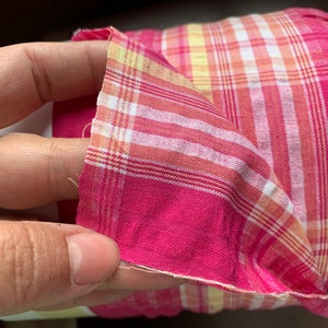 May include: Pink and yellow plaid fabric with a white and yellow plaid pattern. The fabric is folded in half and the edges are frayed.