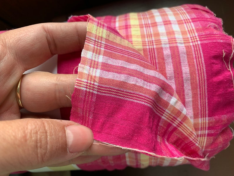 May include: Pink and yellow plaid fabric with a white and yellow plaid pattern. The fabric is folded in half and the edges are frayed.