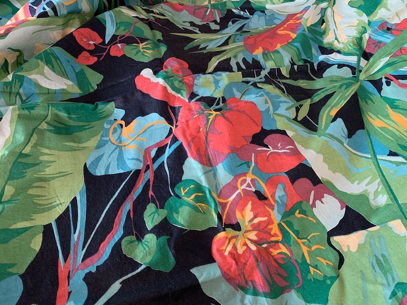 K&ouml;nnte beinhalten: Ein schwarzer Stoff mit einem farbenfrohen tropischen Druck mit gro&szlig;en gr&uuml;nen Bl&auml;ttern, roten und rosa Bl&uuml;ten und gelben Akzenten.