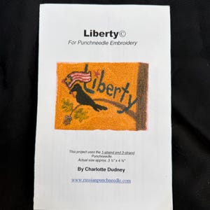 May include: A printed instruction sheet for punchneedle embroidery. The design features the word "Liberty" with a black bird, a waving flag, and a branch on an orange background. The actual size is approximately 3.5" x 4.75".