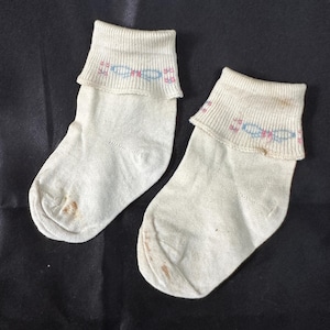 May include: Two pairs of white ankle socks with a small pink and blue design on the cuff.