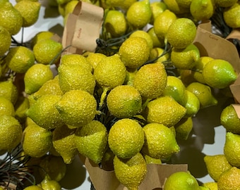 May include: A bunch of small, yellow, artificial lemons with a textured surface. The lemons are arranged in a cluster and are attached to a brown stem. The lemons are surrounded by brown paper with the words "Amitie" and "Culler" written on them.
