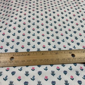May include: White fabric with a repeating pattern of small pink and blue flowers. A wooden ruler is placed on top of the fabric.