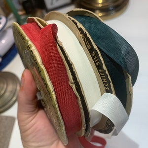 以下が含まれることがあります： 赤、白、緑、白の4つのリボン巻き。リボン巻きには「SCHIFF SILK MILLS」の文字が書かれている。