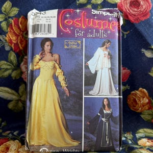 May include: A Simplicity sewing pattern envelope for adult costumes, number 5543, featuring illustrations of three different long-sleeved gowns. The cover displays a yellow dress, a white dress with a lace overlay, and a dark blue dress with a belt.
