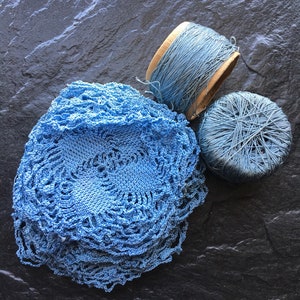 May include: A blue crocheted doily with two spools of blue thread. One spool is in a wooden container.