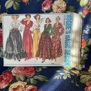 May include: A vintage Vogue's Basic Design sewing pattern packet. The packet features illustrations of five different long skirt and blouse designs. The packet is cream-colored with blue text and is set against a floral background.