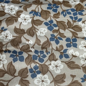 Pode incluir: Um tecido bege com um padrão repetitivo de folhas marrons e flores azuis e brancas.