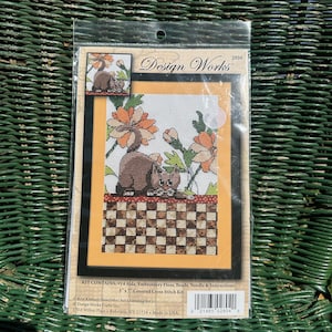 Peut inclure: Un kit de point de croix compté avec deux chats bruns, des fleurs orange et un motif à carreaux. Le kit comprend de l'Aida n° 14, du fil à broder, des perles, une aiguille et des instructions. Le kit mesure 12,7 cm sur 17,8 cm.