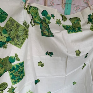 Puede incluir: Mantel de mesa de lino blanco con un patrón repetido verde y blanco de frutas, hojas y cestas. El patrón es de estilo vintage.
