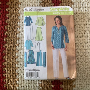 May include: A Simplicity sewing pattern, number 4149, for making a tunic top and pants. The pattern includes instructions for making three different styles of tops, all with long sleeves. The model is wearing a blue and white patterned tunic top with white pants. The pattern is labeled "easy-to-sew".