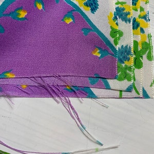 Pu&ograve; includere: Primo piano di un mucchio di ritagli di tessuto con un motivo floreale in tonalit&agrave; di viola, bianco, verde e giallo. Il tessuto &egrave; sfilacciato ai bordi.