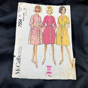 May include: Vintage McCall's sewing pattern for a misses' robe. The pattern number is 7554, size medium (14-16). The pattern includes three different styles of robes: one with a floral print, one in a solid pink, and one in a solid yellow.