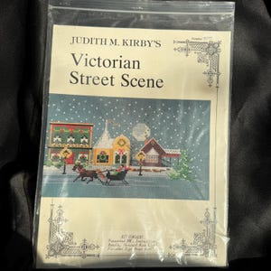 Könnte beinhalten: Ein Kreuzstich-Set mit dem Titel "Victorian Street Scene" von Judith M. Kirby. Das Bild zeigt eine Winterszene mit Gebäuden, einer Pferdekutsche und Schnee. Das Set enthält DNC, Anweisungen, eine Nadel und 14-Count-Aida-Stoff. Fertige Größe ca. 15 x 41 cm.