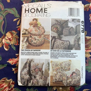 May include: A McCall's Home Decorating pattern envelope featuring a floral design. The pattern is for a tapestry tote bag, cushion, and magazine holder. The pattern number is 6778. The text on the envelope reads "The Touch of Tapestry" and "Le Luxe de la Tapisserie".