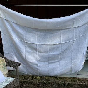 May include: A white linen sheet hanging on a washing line outdoors. The sheet is slightly creased and has a small dark mark in the centre.