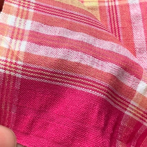 May include: Pink and white plaid fabric with thin yellow stripes. The fabric is woven and has a soft texture.