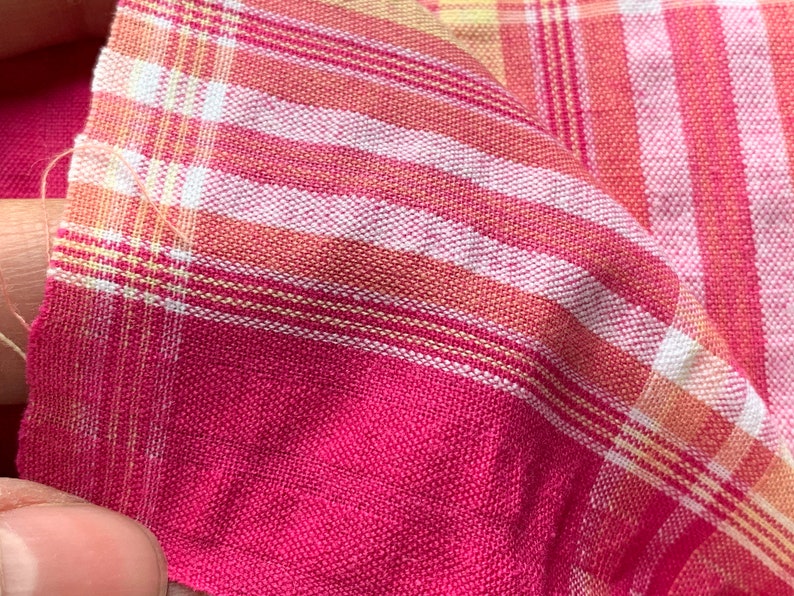 May include: Pink and white plaid fabric with thin yellow stripes. The fabric is woven and has a soft texture.