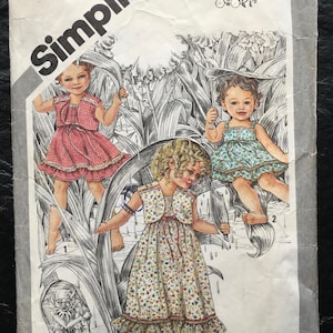 Może przedstawiać: Wzorzec szycia Simplicity vintage dla sukienek dla dzieci. Wzorzec jest dla trzech różnych sukienek, każda z innym nadrukiem kwiatowym. Wzorzec nosi tytuł "Kopciuszek" i zawiera instrukcje dla rozmiarów 2-14.
