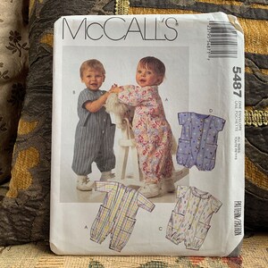 May include: McCall's sewing pattern number 5487 for a baby's one-piece outfit. The pattern includes four different styles: a striped one-piece, a floral one-piece, a blue one-piece with white polka dots, and a yellow and blue one-piece with a floral pattern.