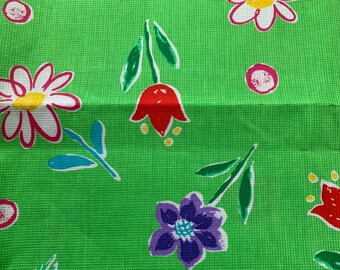 May include: Green fabric with a white, red, blue, and purple floral pattern. The flowers are stylized and have a whimsical look.