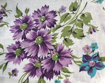 Pode incluir: Tecido estampado floral roxo e azul sobre fundo branco. O tecido apresenta um grupo de flores roxas com folhas verdes e flores menores azuis e roxas.