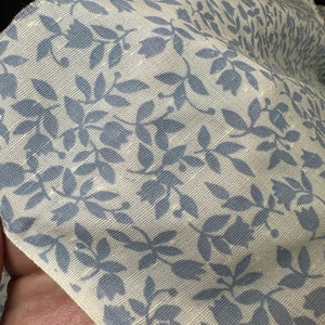 May include: Close-up of a white fabric with a blue floral pattern. The fabric has a subtle texture and the floral design is repeated throughout the fabric.