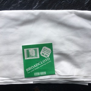 以下が含まれることがあります： 緑色の値札が付いた白いブロードクロス生地。値札には「D/119 C/110 SKU 21319 TOTAL PRICE $6.00 BROADCLOTH for your home sewing needs $2.00 3 YDS」と記載されています。