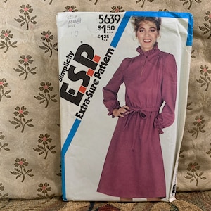 Può includere: Modello Simplicity numero 5639 per un abito con colletto alto, maniche lunghe e cintura annodata. Il modello è per le taglie 10-18 ed è etichettato "Extra-Sure Pattern".