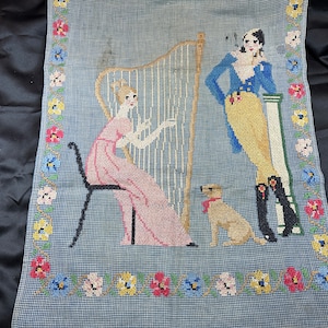 May include: A vintage needlepoint wall hanging depicting a woman playing a harp, a man in a blue jacket and yellow trousers, and a small dog. The scene is framed by a border of colourful flowers.