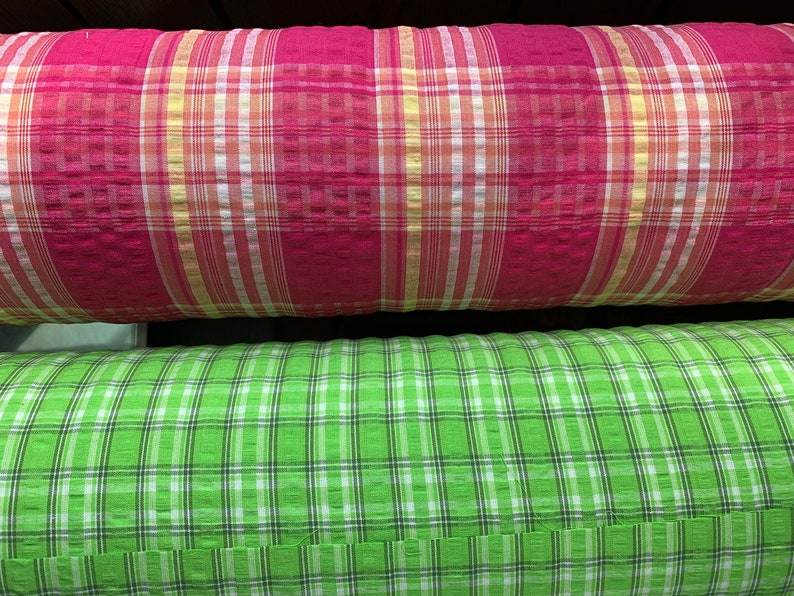 May include: Two rolls of fabric with plaid patterns. The top roll is red with white and yellow stripes. The bottom roll is green with white and black stripes.