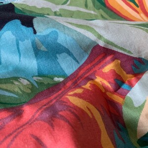 K&ouml;nnte beinhalten: Nahaufnahme eines bunten Stoffes mit tropischem Muster. Der Stoff zeigt gro&szlig;e, abstrakte Bl&auml;tter in Gr&uuml;n-, Blau-, Rot- und Gelbt&ouml;nen.