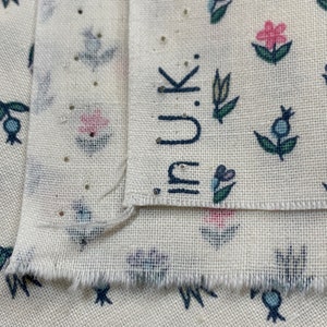 May include: Close-up of two pieces of white fabric with a floral pattern. The fabric has a small, repeating pattern of blue, green, and pink flowers. The top piece of fabric has the word "inuk" printed on it in black.