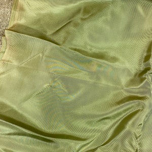 May include: A close-up of a smooth, green fabric with a subtle sheen. The fabric is folded and has a slight wrinkle.