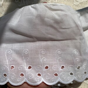May include: White cotton lace trim with a scalloped edge and embroidered floral designs. The lace has a delicate, feminine look.