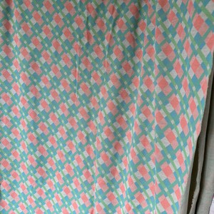 Puede incluir: Una tela a cuadros rosa y verde con un patr&oacute;n de diamante. La tela est&aacute; doblada y colgada en una pared.