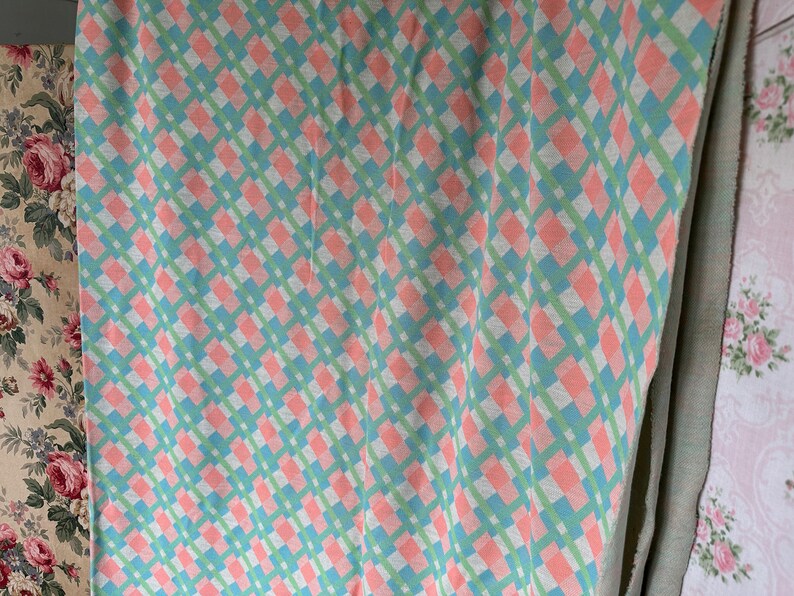 Puede incluir: Una tela a cuadros rosa y verde con un patr&oacute;n de diamante. La tela est&aacute; doblada y colgada en una pared.