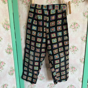 May include: Black pants with a colorful geometric pattern. The pattern is made up of squares in shades of red, yellow, blue, and green.