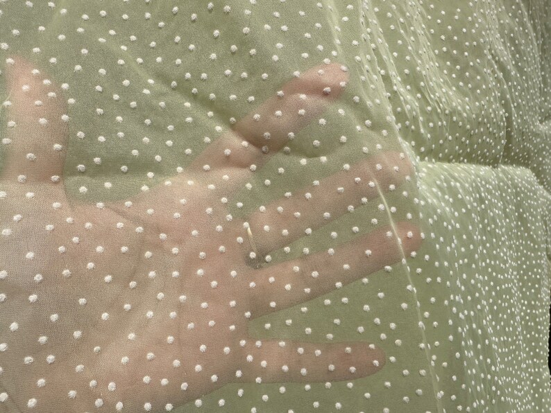 May include: A sheer green fabric with white polka dots. The fabric is translucent and has a soft, delicate texture.