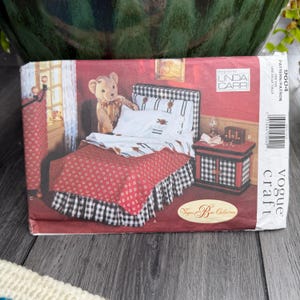 Puede incluir: Un patrón de Vogue Craft para un juego de dormitorio en miniatura. El patrón presenta una cama con un edredón estampado en rojo y blanco y una falda de cama a cuadros en blanco y negro. Un oso de peluche está en la cama. El patrón está diseñado por Linda Carr.