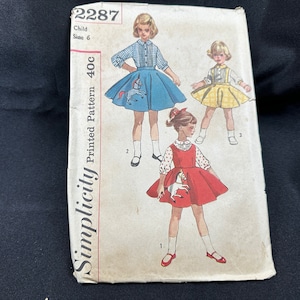 Könnte beinhalten: Simplicity Printed Pattern 40c Schnittmuster für ein Kinderkleid. Das Schnittmuster zeigt drei Mädchen, die verschiedene Versionen des Kleides tragen. Das Kleid hat ein Pferdemotiv auf der Vorderseite. Die Schnittmuster-Nummer ist 2287.