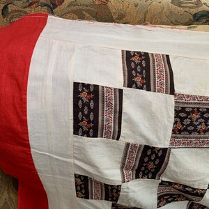 May include: A patchwork quilt with a red border and a white background. The quilt is made of squares of different fabrics with floral patterns in brown, white, and red.
