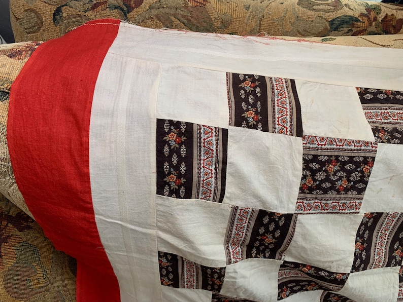 May include: A patchwork quilt with a red border and a white background. The quilt is made of squares of different fabrics with floral patterns in brown, white, and red.