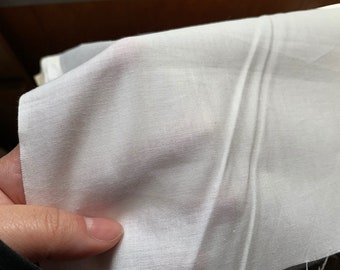 Könnte beinhalten: Ein Stück weißer Stoff mit einem feinen, halbtransparenten Gewebe. Das Material hat eine glatte Textur und eine leichte Lichtdurchlässigkeit, wodurch Licht durch die Fasern scheinen kann. Der Stoff ist gefaltet und bildet weiche Falten.