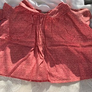 以下が含まれることがあります： 花柄のプリントが施されたピンクの綿のドレス。ドレスはフリルネックと短い袖です。