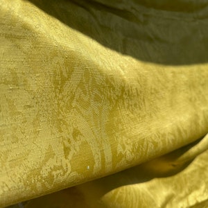 May include: A close-up of a yellow fabric with a subtle, embossed pattern. The fabric has a soft, silky texture and a slightly wrinkled appearance.