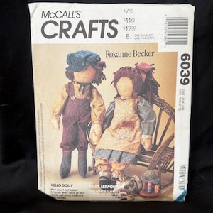Puede incluir: Patrón de McCall's Crafts con dos muñecas hechas a mano, Violet y Albert, diseñadas por Roxanne Becker. El patrón incluye instrucciones para hacer muñecas de 60 cm con ropa completa. La portada muestra las muñecas y el texto "Hola Dolly."