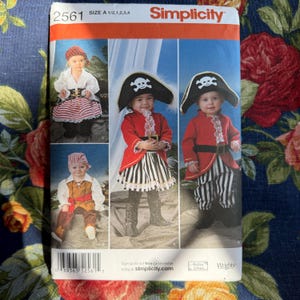 May include: Simplicity sewing pattern 2561 for children's pirate costumes. The pattern features images of the costumes, including red jackets, striped skirts and trousers, and pirate hats with skull and crossbones. Size A 1/2, 1, 2, 3, 4.