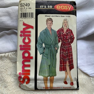 May include: Simplicity sewing pattern number 5249 for a robe. The pattern includes instructions for making a robe for both men and women. The pattern is for sizes S-XXL. The pattern cover features a photo of two people wearing robes. The woman is wearing a red and white plaid robe and the man is wearing a green robe.